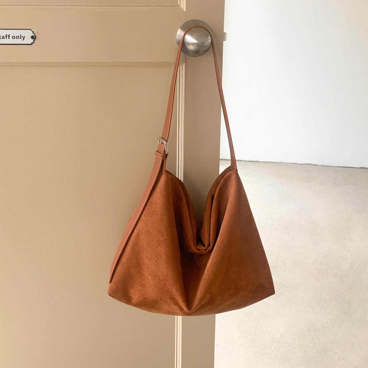 Sloane Suede Hobo Bag in tan, hanging on a door
